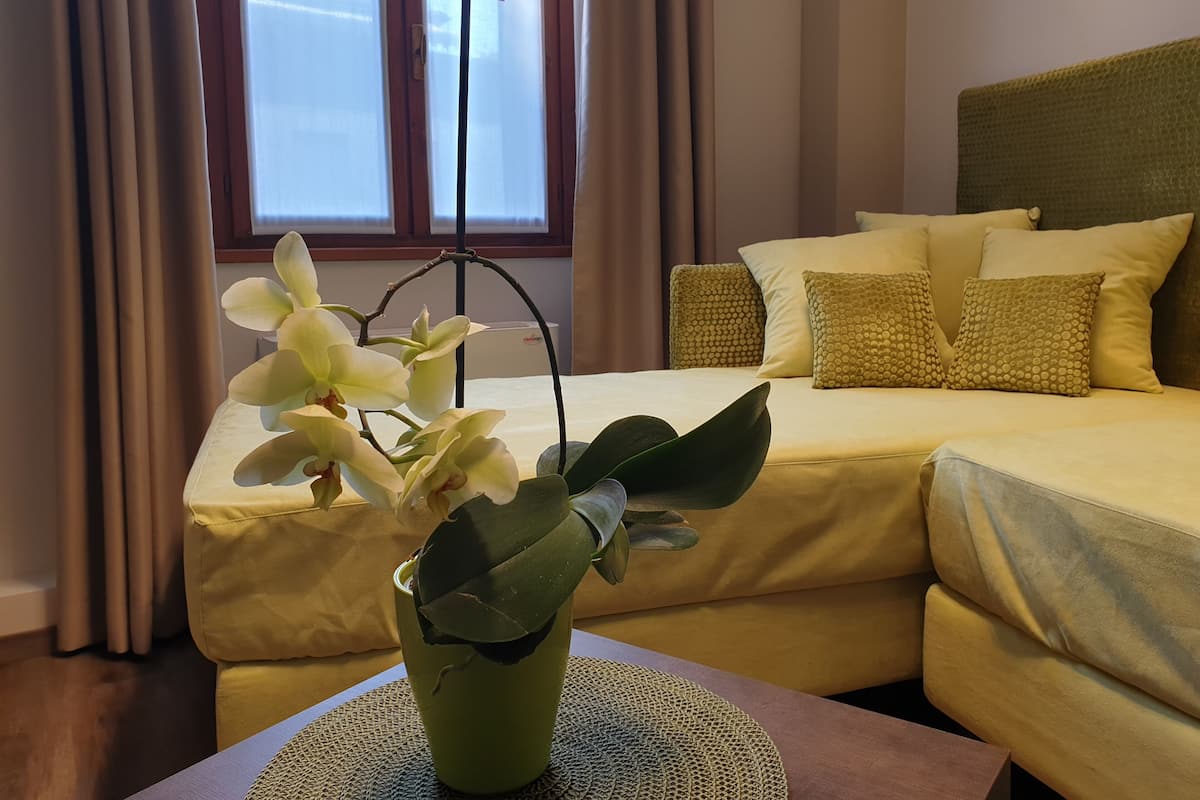 A hotel room with a bed, a bedside table with a vase of flowers, and a window with curtains.