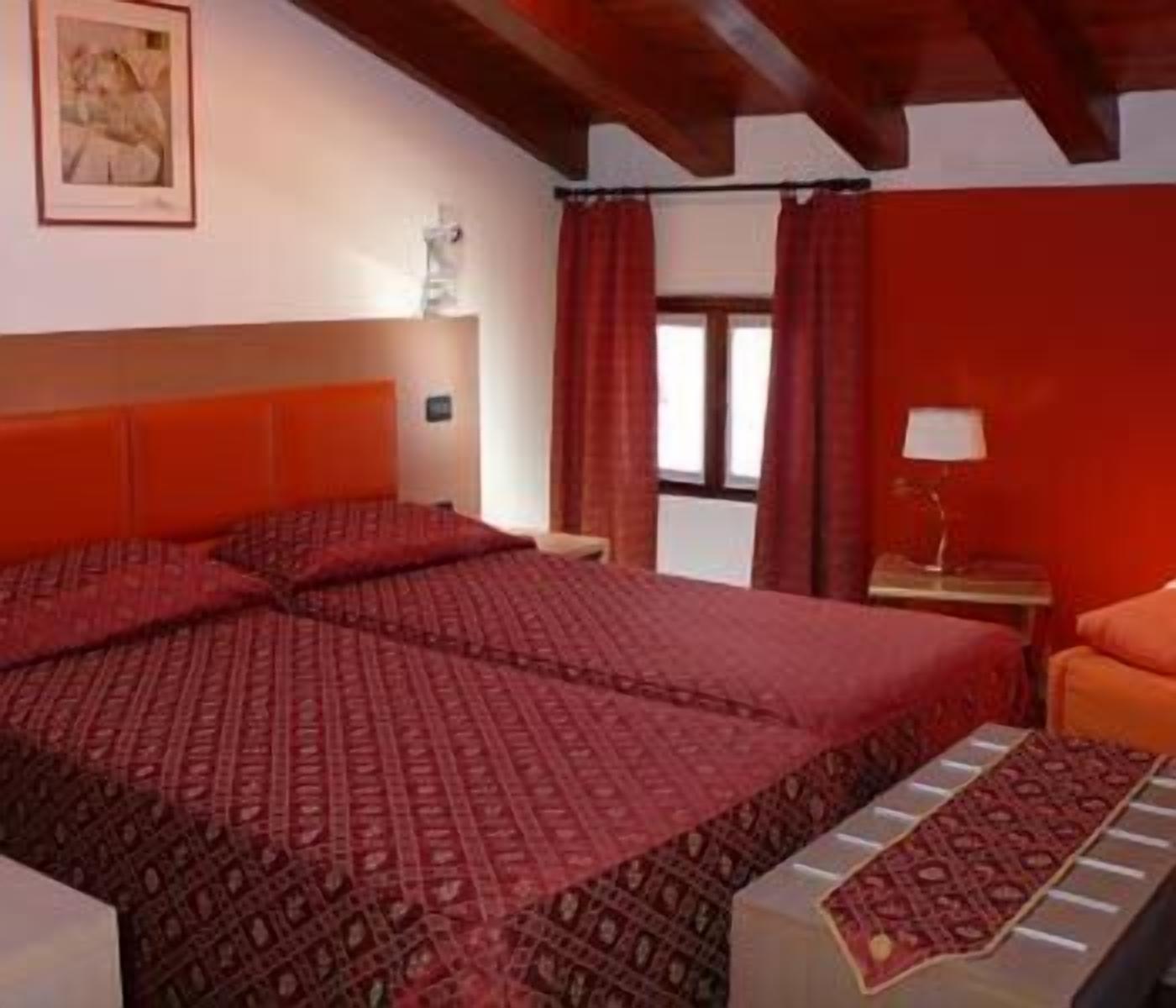 A hotel room with a large bed, a nightstand, a lamp, and a window with curtains.