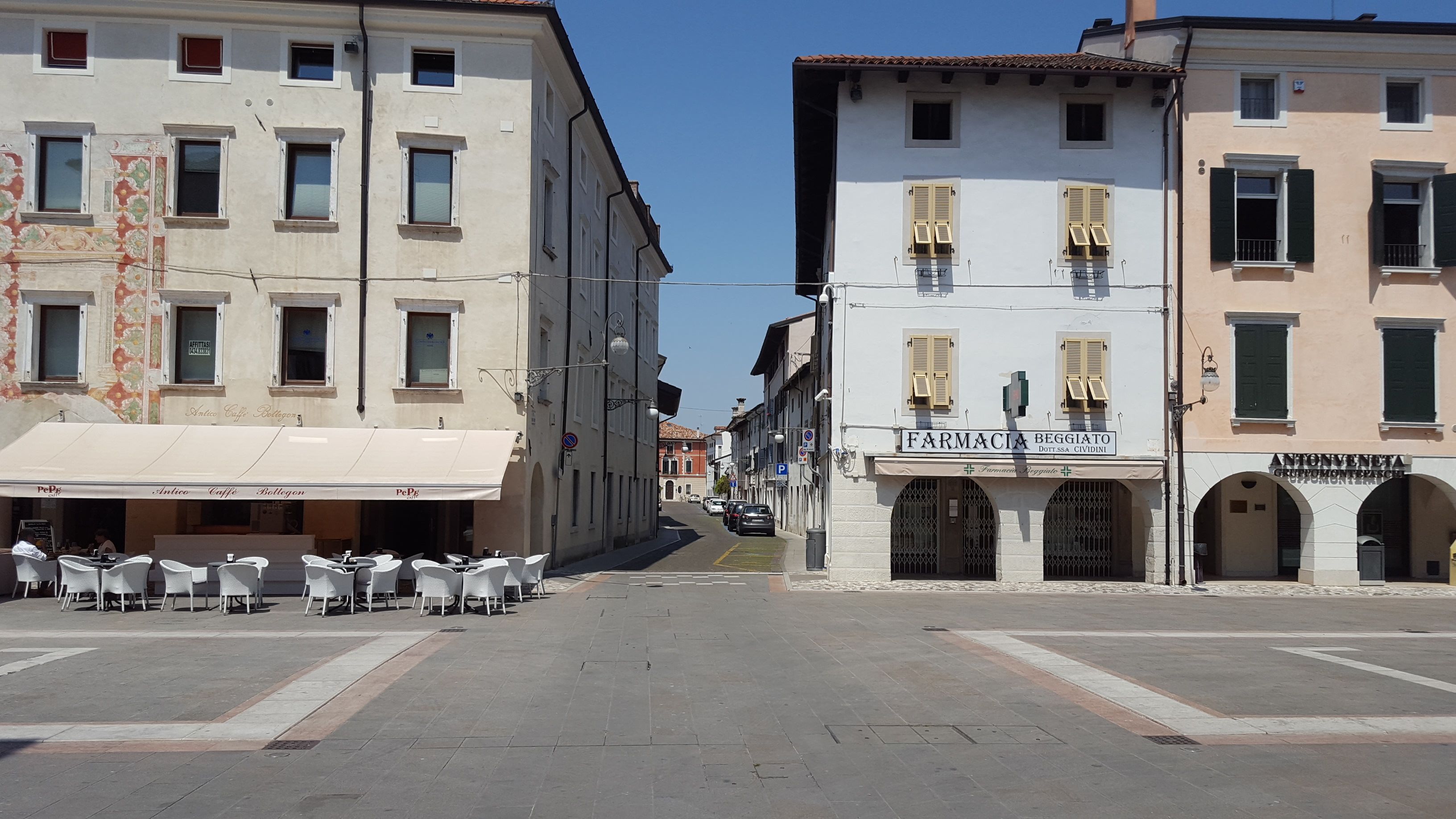 Une rue avec des terrasses et une pharmacie.