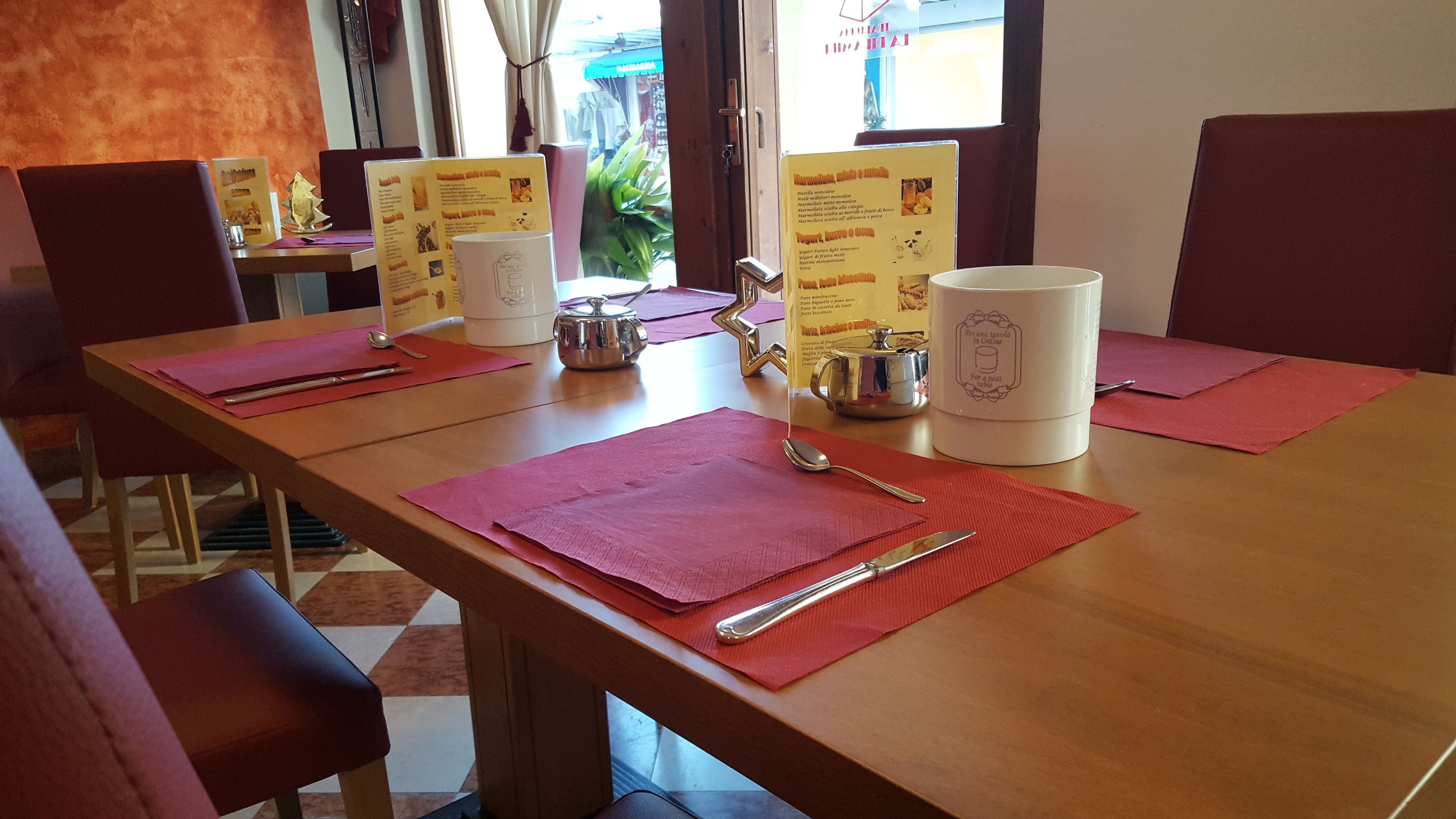 Een eettafel gedekt met rode placemats, bestek en een witte karaf.