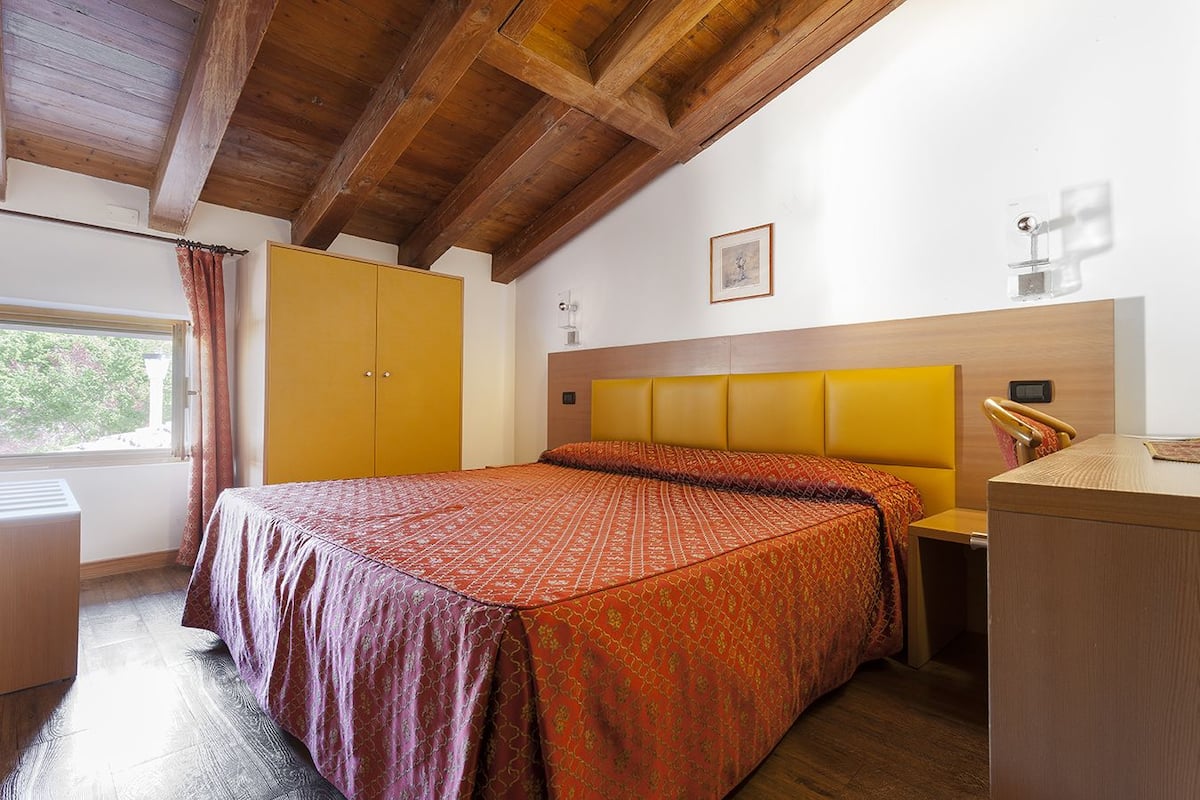 A bedroom with a bed, a wardrobe, a bedside table, and a window.