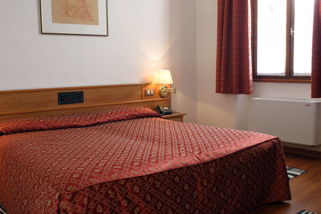 A hotel room with a bed, a bedside lamp, a telephone, and a window with curtains.