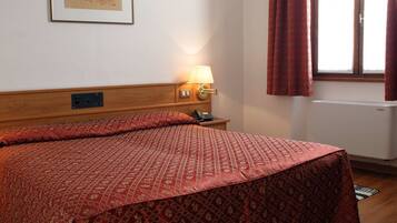 A hotel room with a bed, a bedside lamp, a telephone, and a window with curtains.