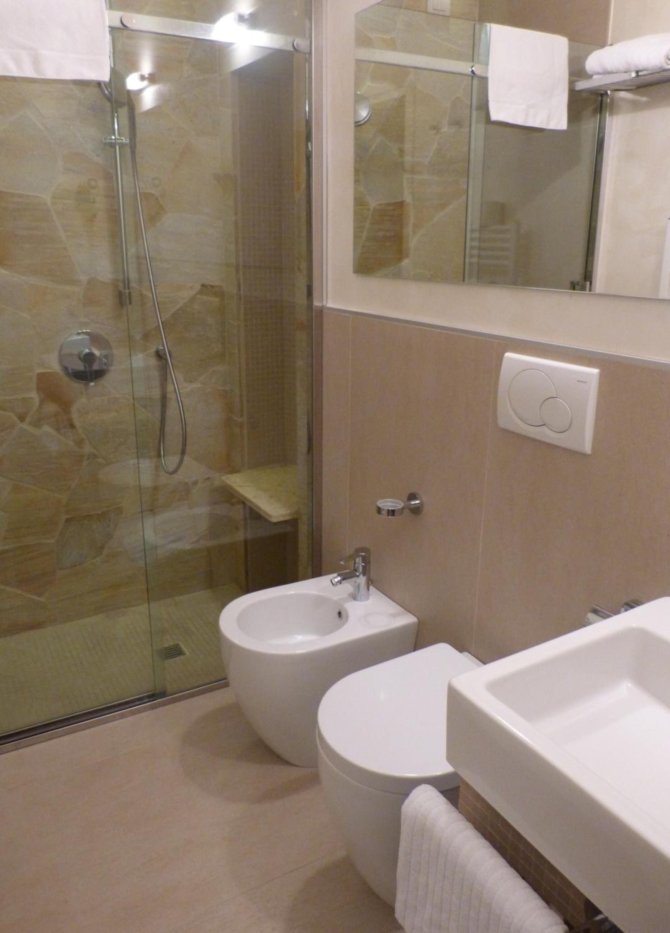 A bathroom with a glass shower enclosure, a bidet, a toilet, and a sink.