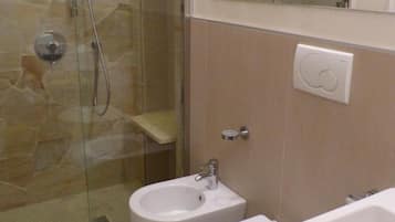 A bathroom with a glass shower enclosure, a bidet, a toilet, and a sink.