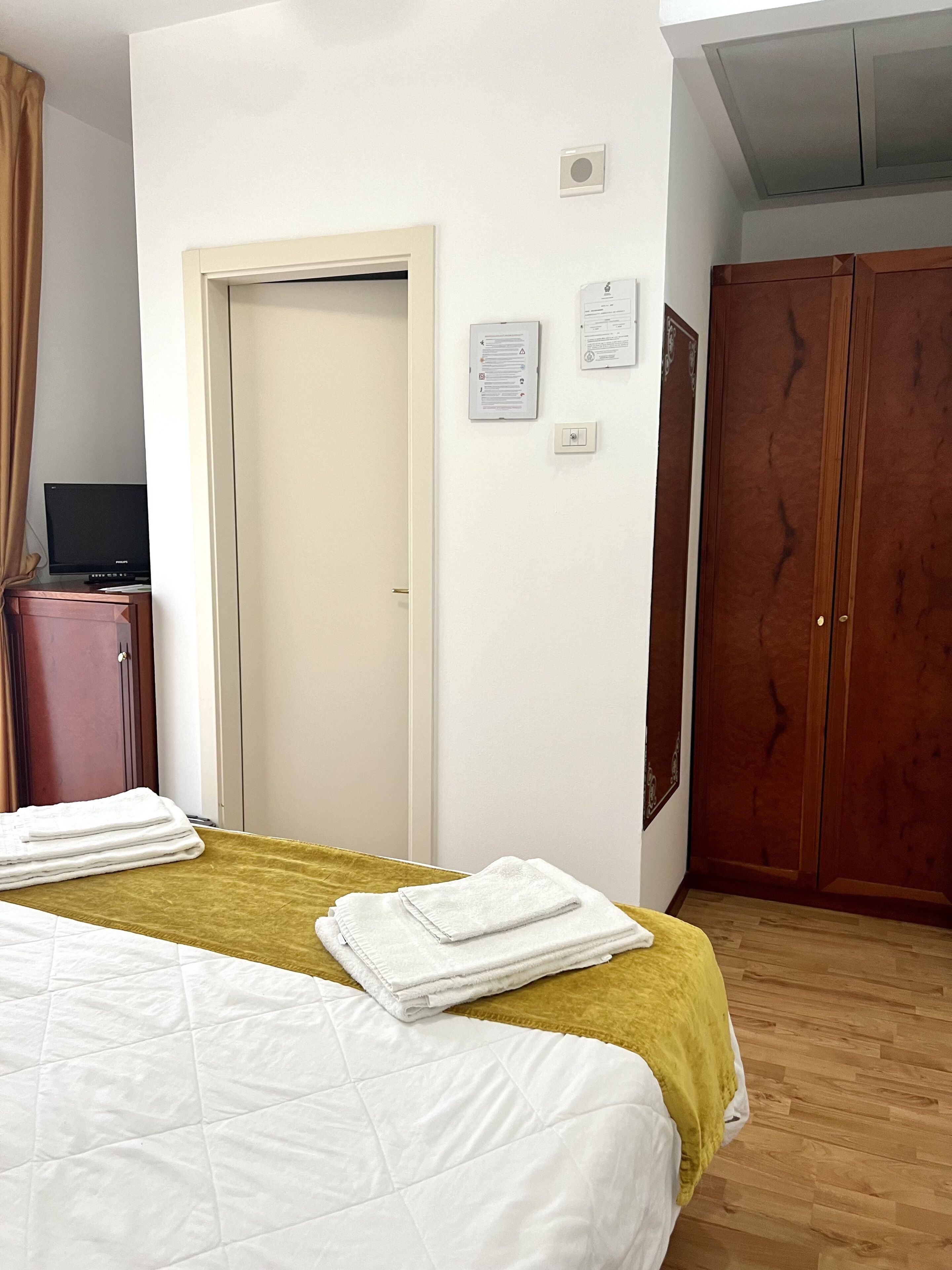 Una camera d'albergo con un letto, un armadio, una televisione su un mobile e una porta.