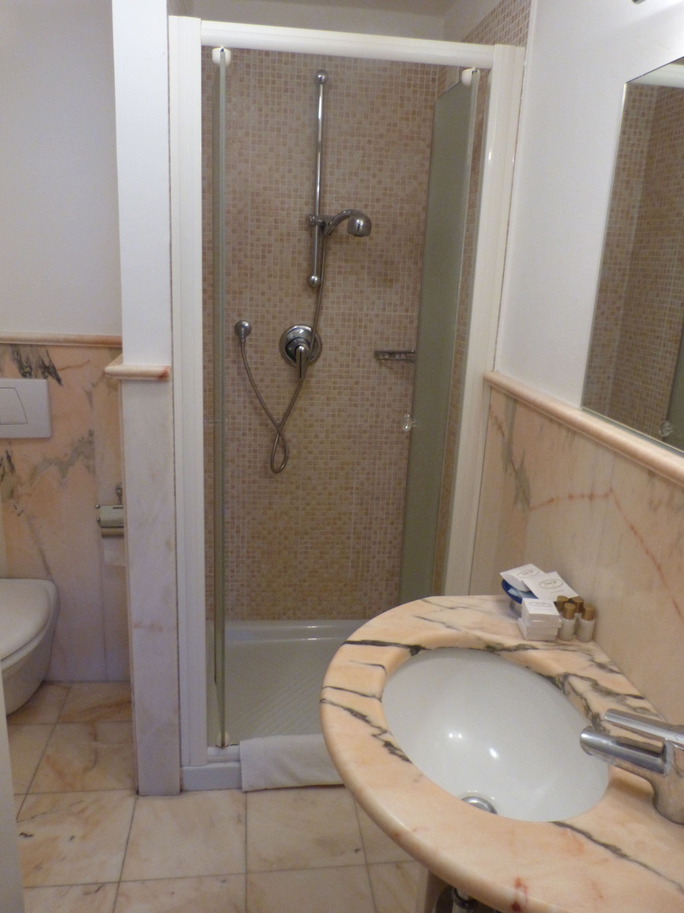 Un baño con ducha de vidrio, lavamanos de mármol y retrete.