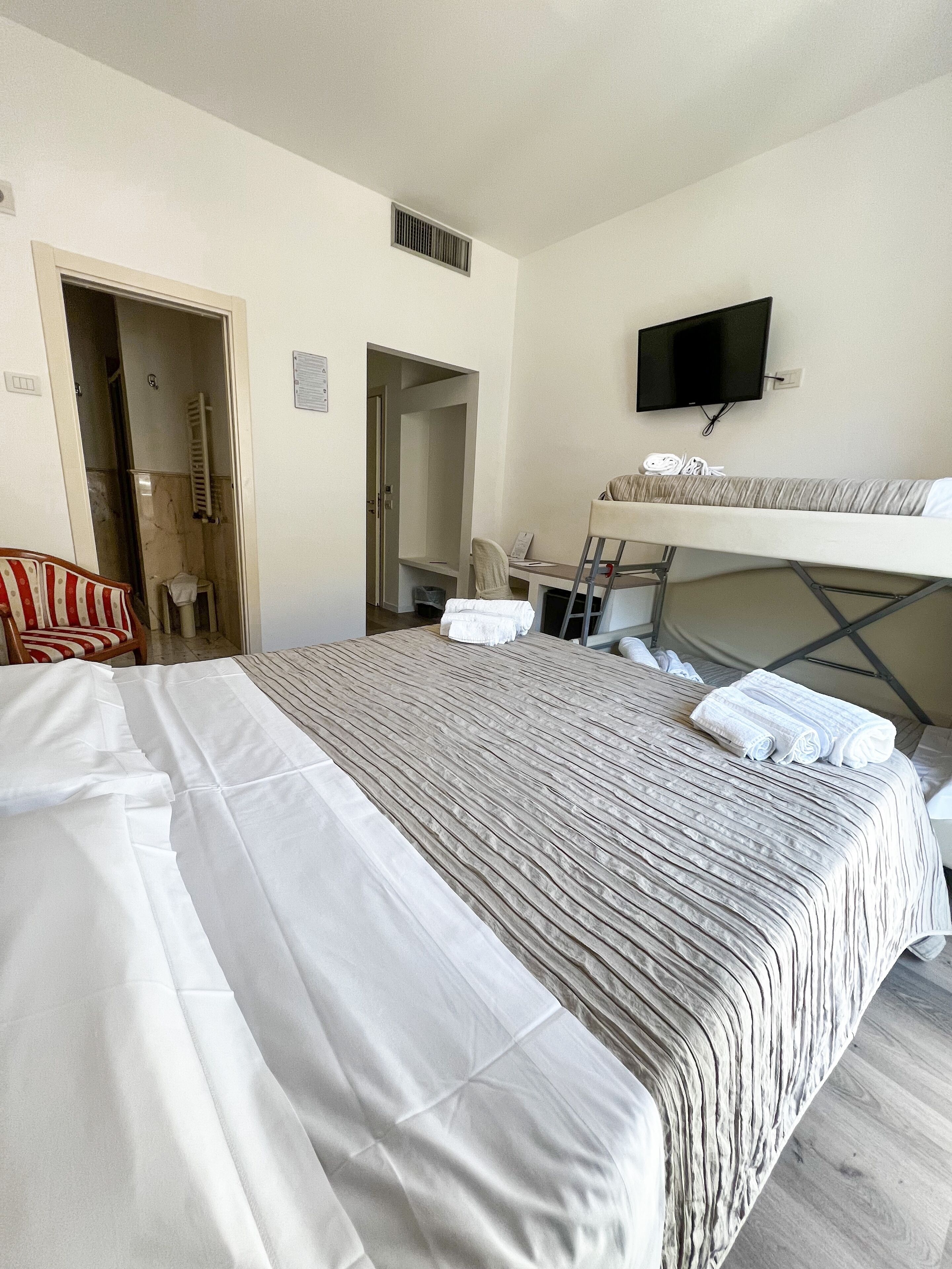 Una habitación de hotel con cama, televisor montado en la pared, una silla y un escritorio.