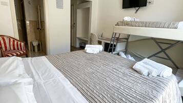 Una habitación de hotel con cama, televisor montado en la pared, una silla y un escritorio.