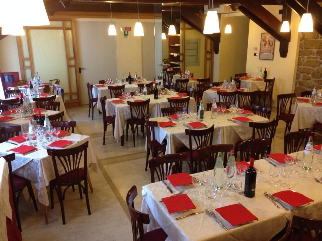 A restaurant with multiple round tables set with red napkins, wine glasses, and bottles.