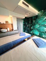 A modern bedroom with a large bed, a built-in sink, and a green leaf-patterned wall.