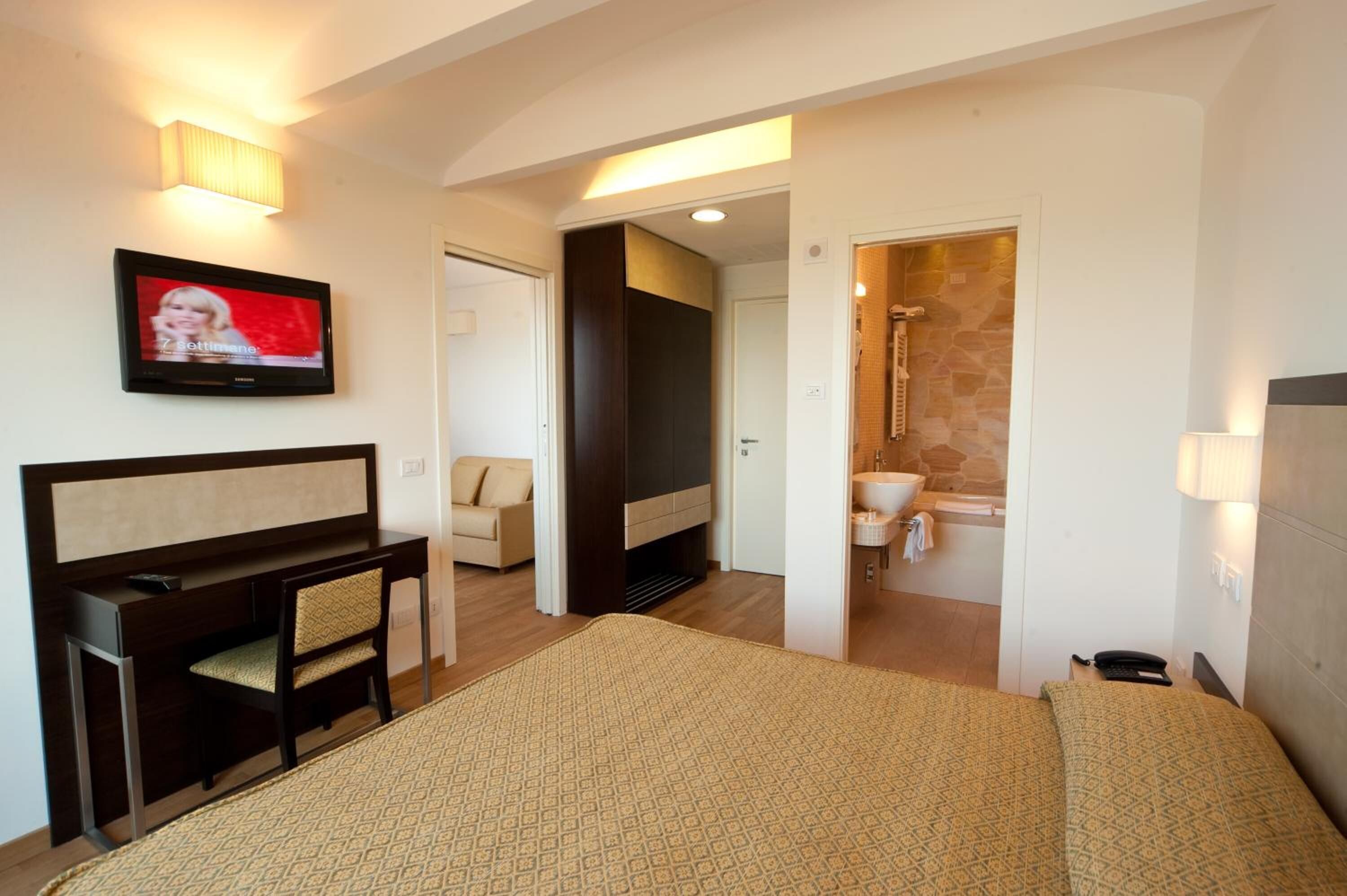 A hotel room with a bed, a desk, a TV, a sofa, a bathroom with a shower, and a small sitting area.