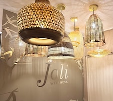 Un centro de bienestar con varias lámparas de mimbre colgantes y una pared con el logotipo de 'Joli Wellness'.