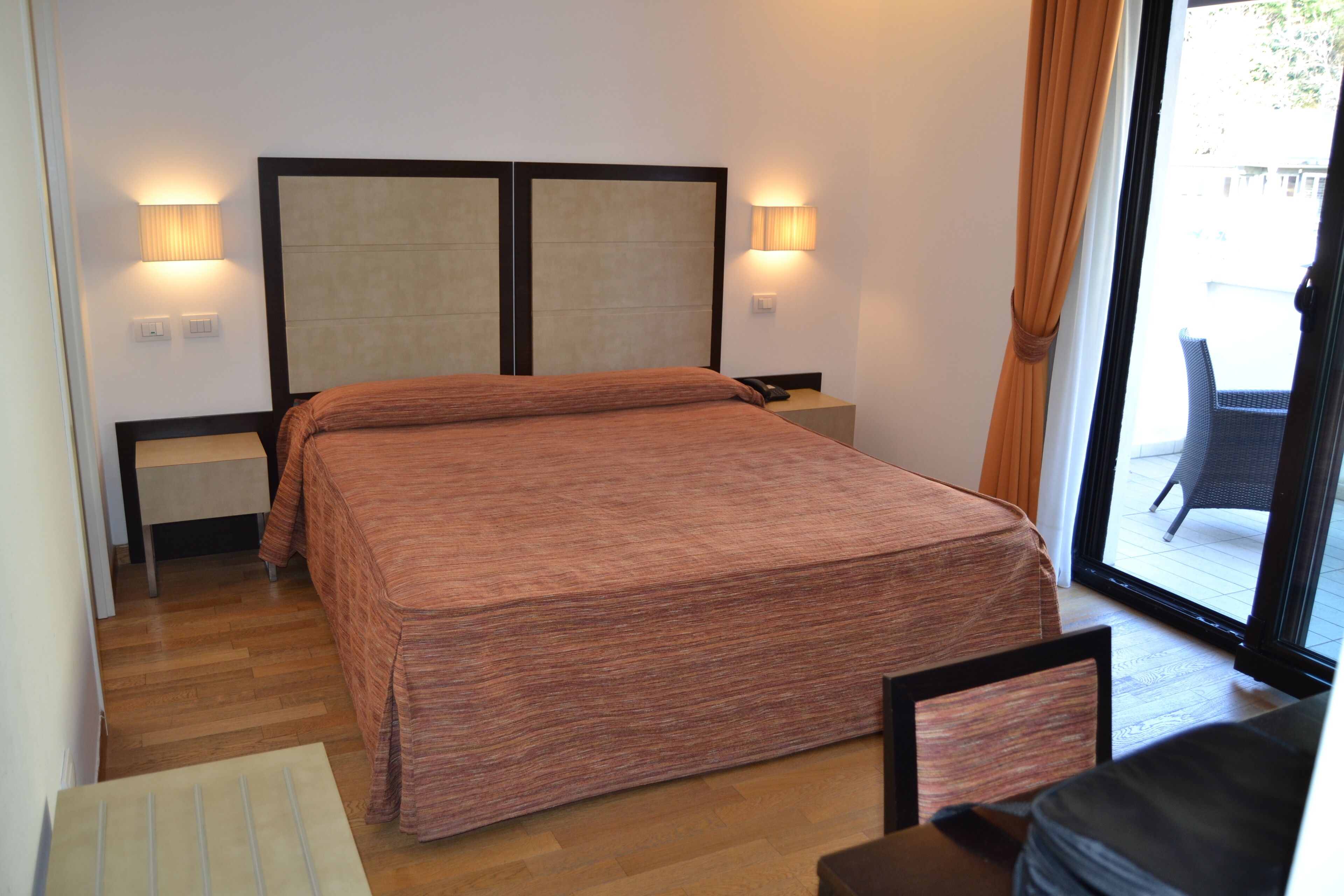 Habitación de hotel con una cama grande, dos lámparas de noche, una mesita de noche y vistas al exterior a través de un ventanal.
