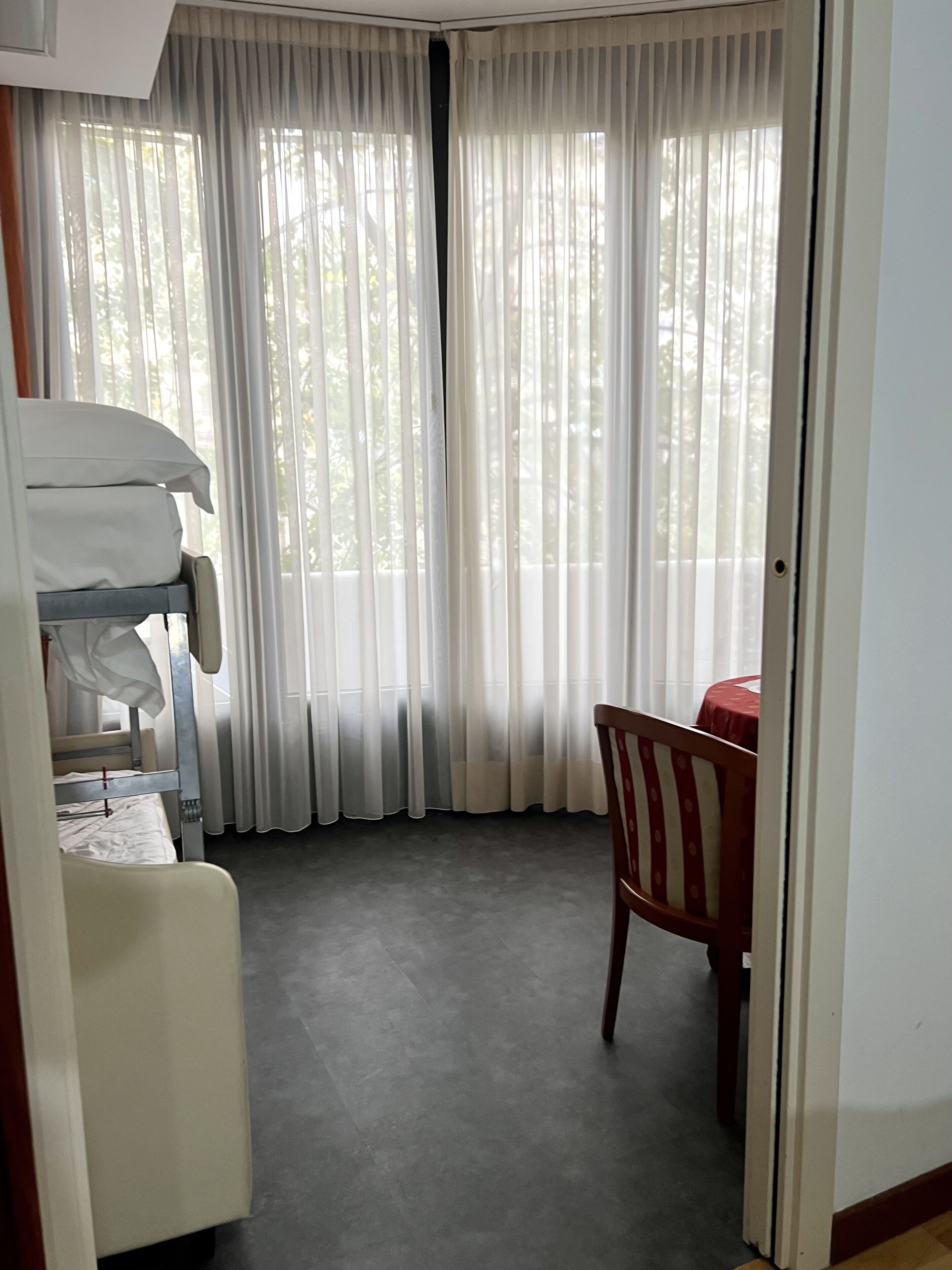 Una habitación de hotel con una cama litera, una silla de madera y una mesa con mantel rojo.