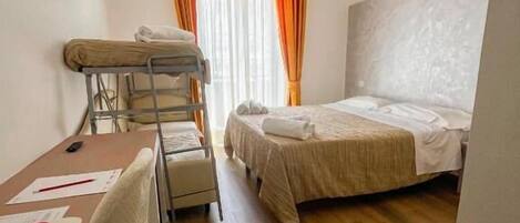 Une chambre d’hôtel de taille réduite, avec un lit superposé, un bureau avec des papiers et une chaise.