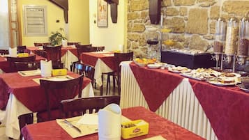 Un restaurante con paredes de piedra y vigas de madera, mesas con manteles rojos y un bufé con diversas opciones de comida.