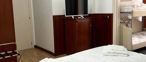 Une chambre d’hôtel avec un lit, un téléviseur posé sur une commode en bois, un lit superposé et un plancher en bois.