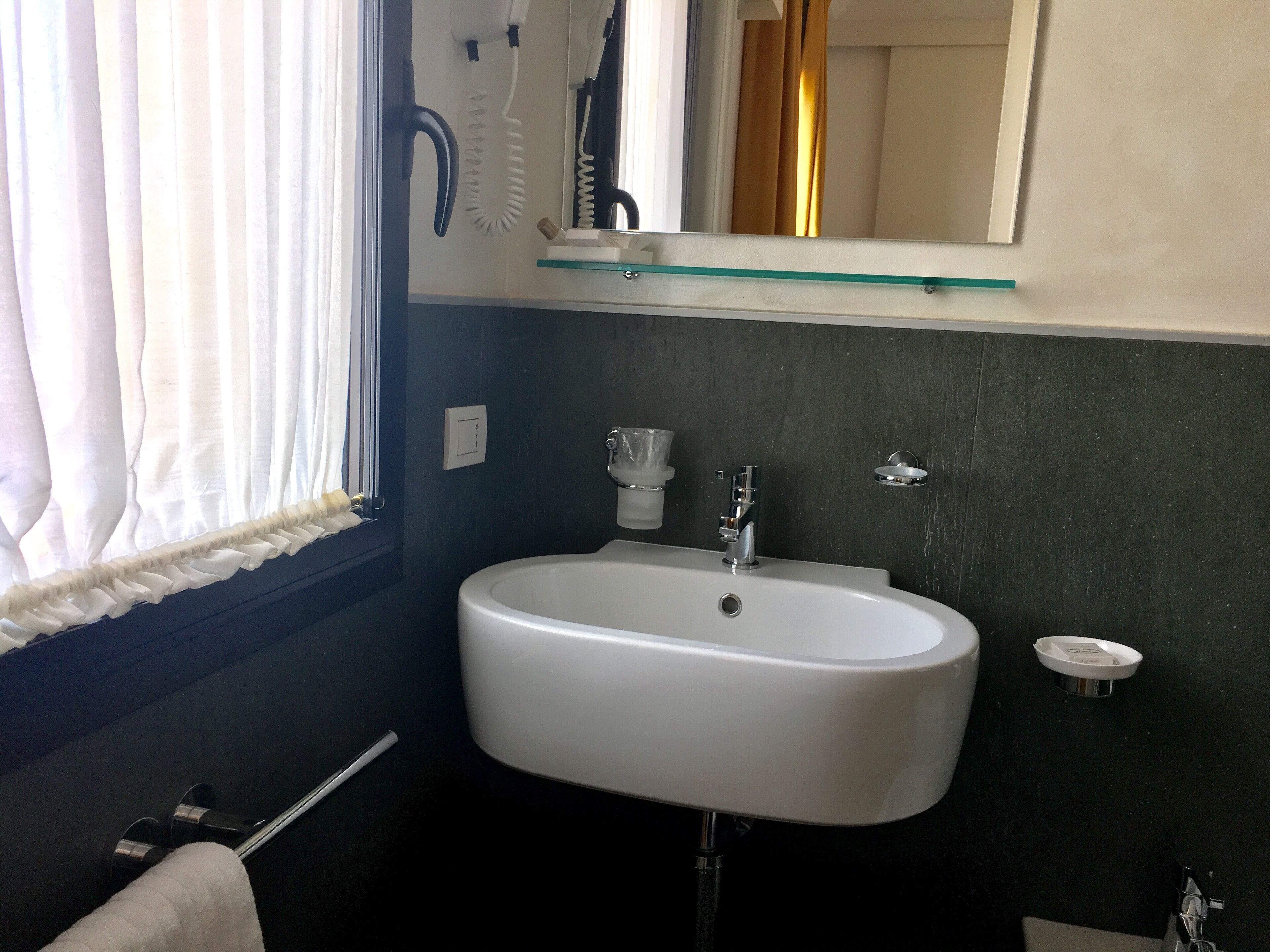 A bathroom with a white sink, a mirror above it, and a window with curtains.