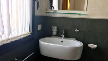 A bathroom with a white sink, a mirror above it, and a window with curtains.