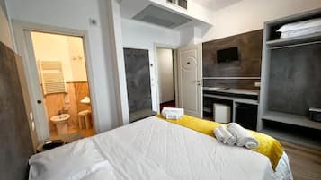 A modern hotel room with a large bed, a bathroom with a sink and toilet, a TV mounted on the wall, and a wardrobe.