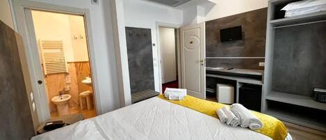 A modern hotel room with a large bed, a bathroom with a sink and toilet, a TV mounted on the wall, and a wardrobe.