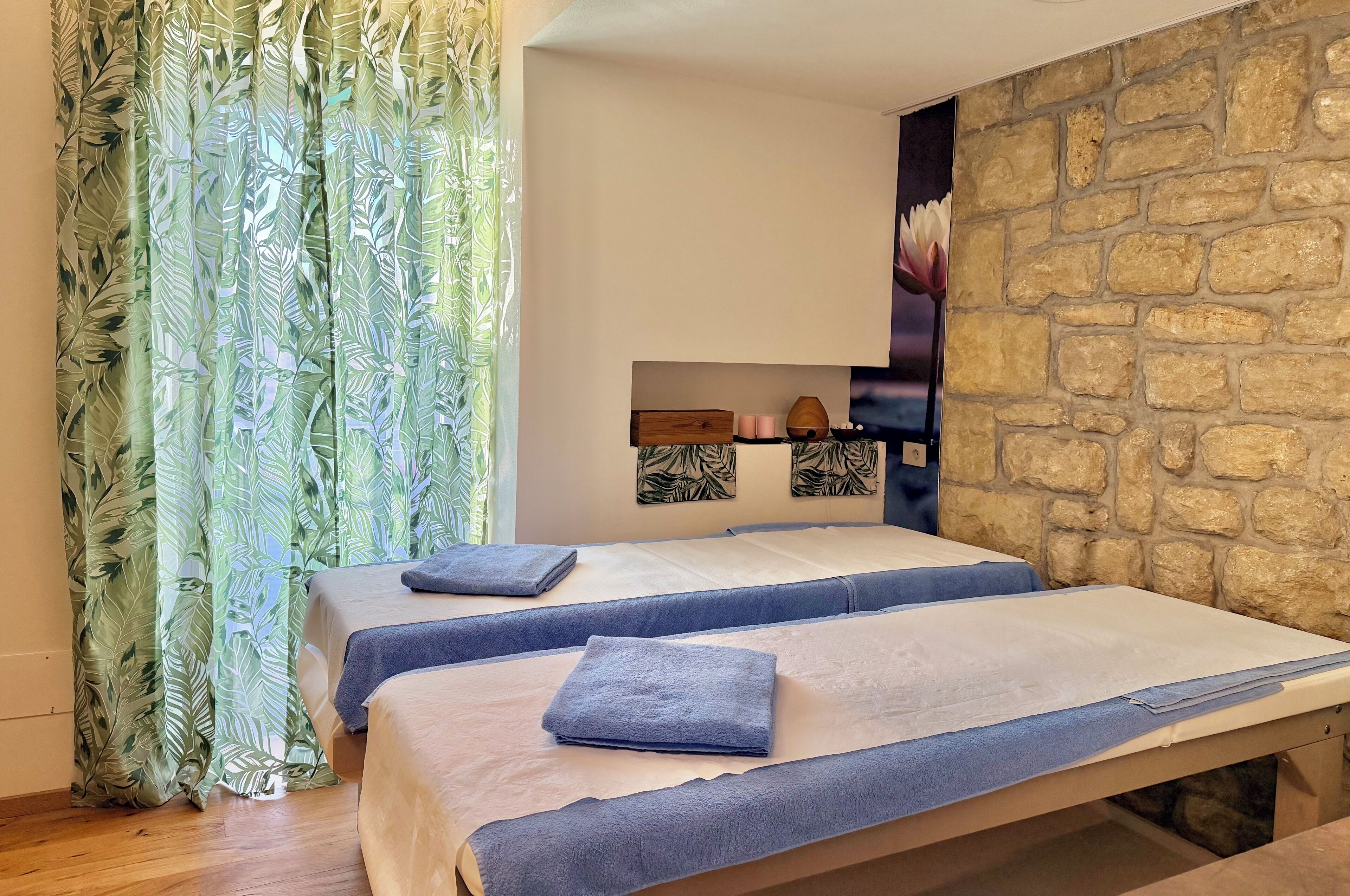 A room with two beds, a stone wall, and a floral curtain.