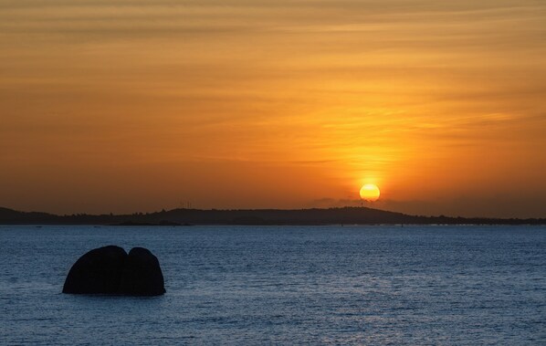 A sunset over a body of water with a silhouette of a landmass in the distance.