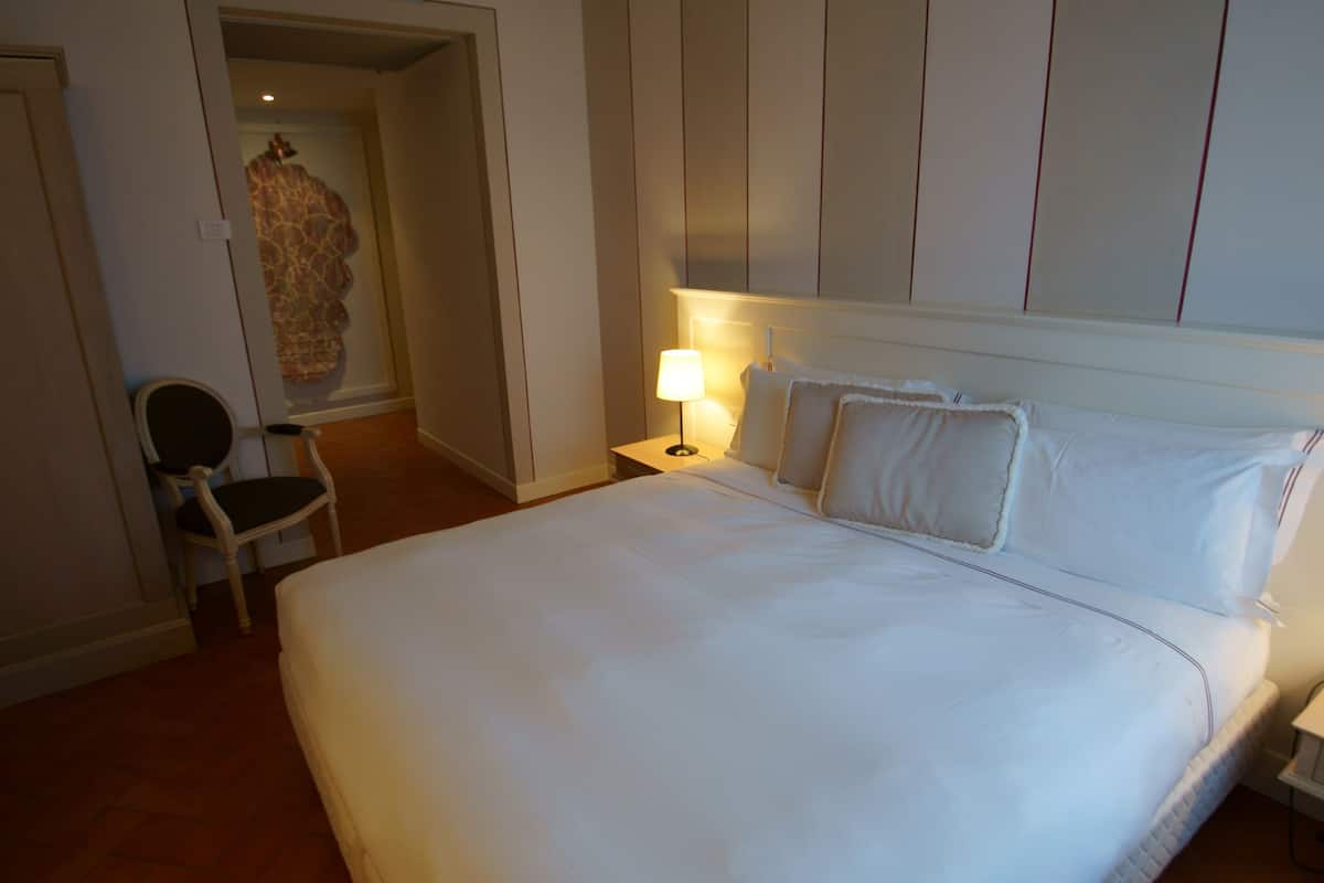 Une chambre d’hôtel avec un grand lit, une table de chevet avec une lampe, une chaise et une œuvre d’art accrochée au mur.