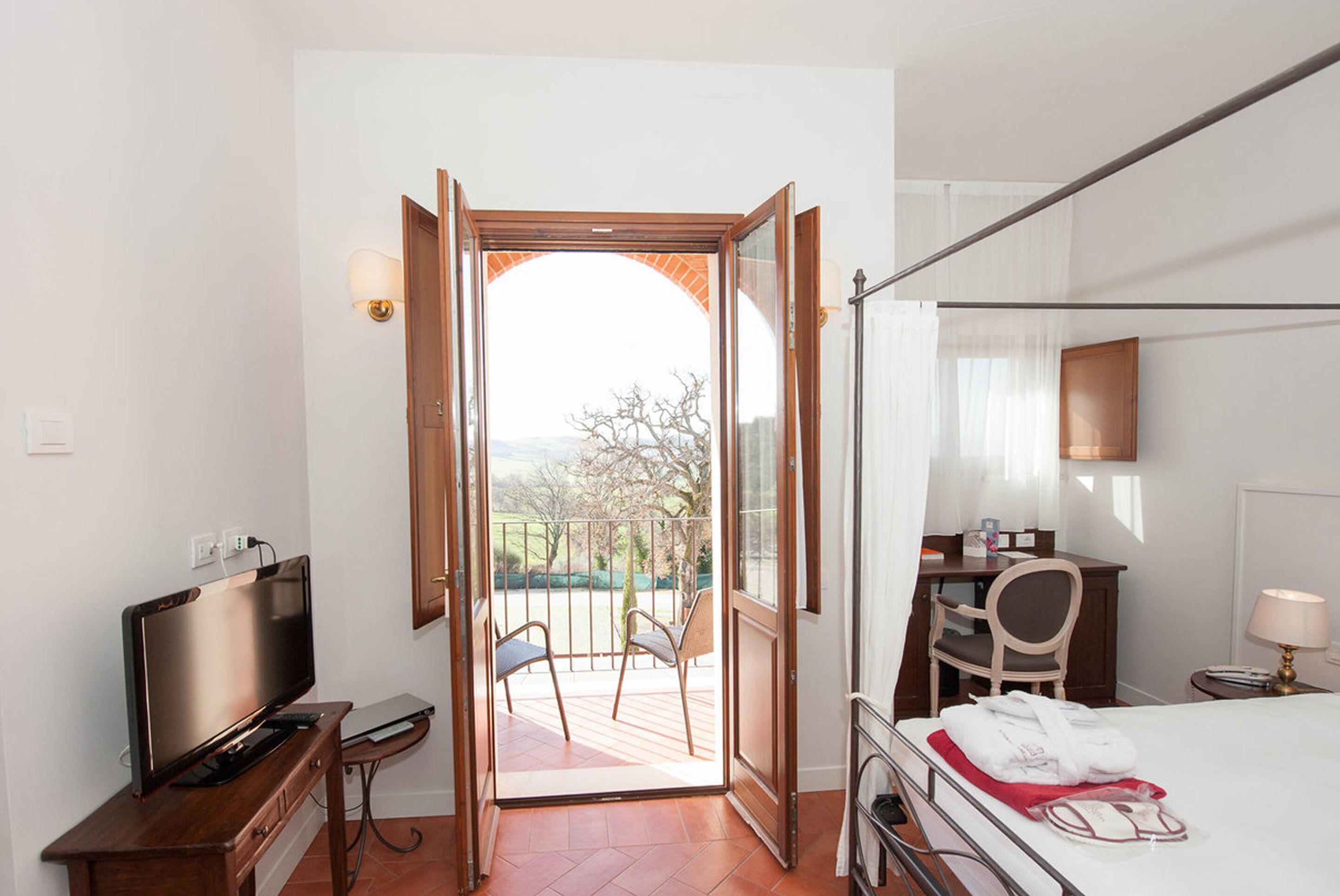 Habitación de hotel con televisión, escritorio, silla, cama y balcón con vistas.