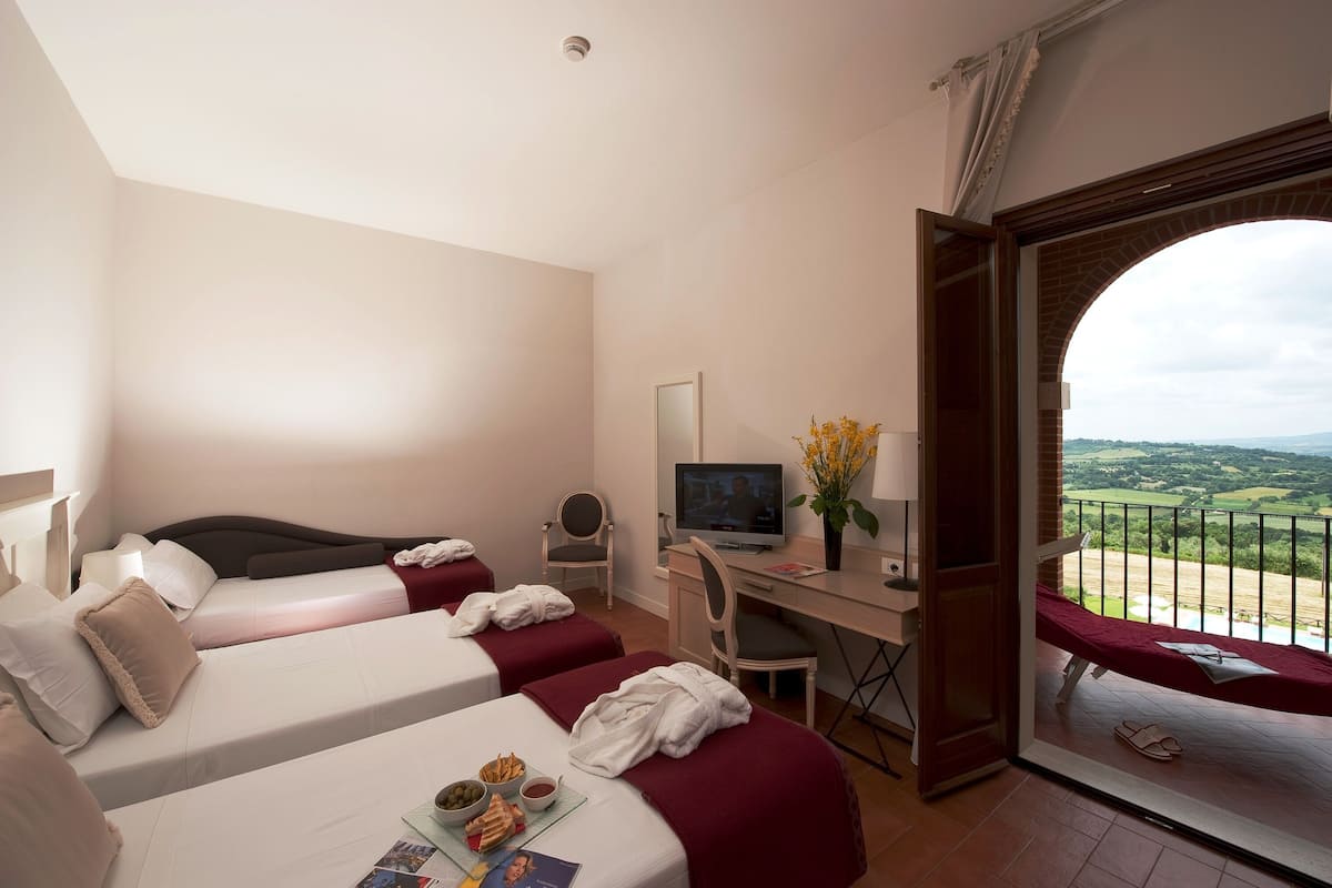 Une chambre d’hôtel avec deux lits, un bureau avec une télévision et un balcon avec vue.