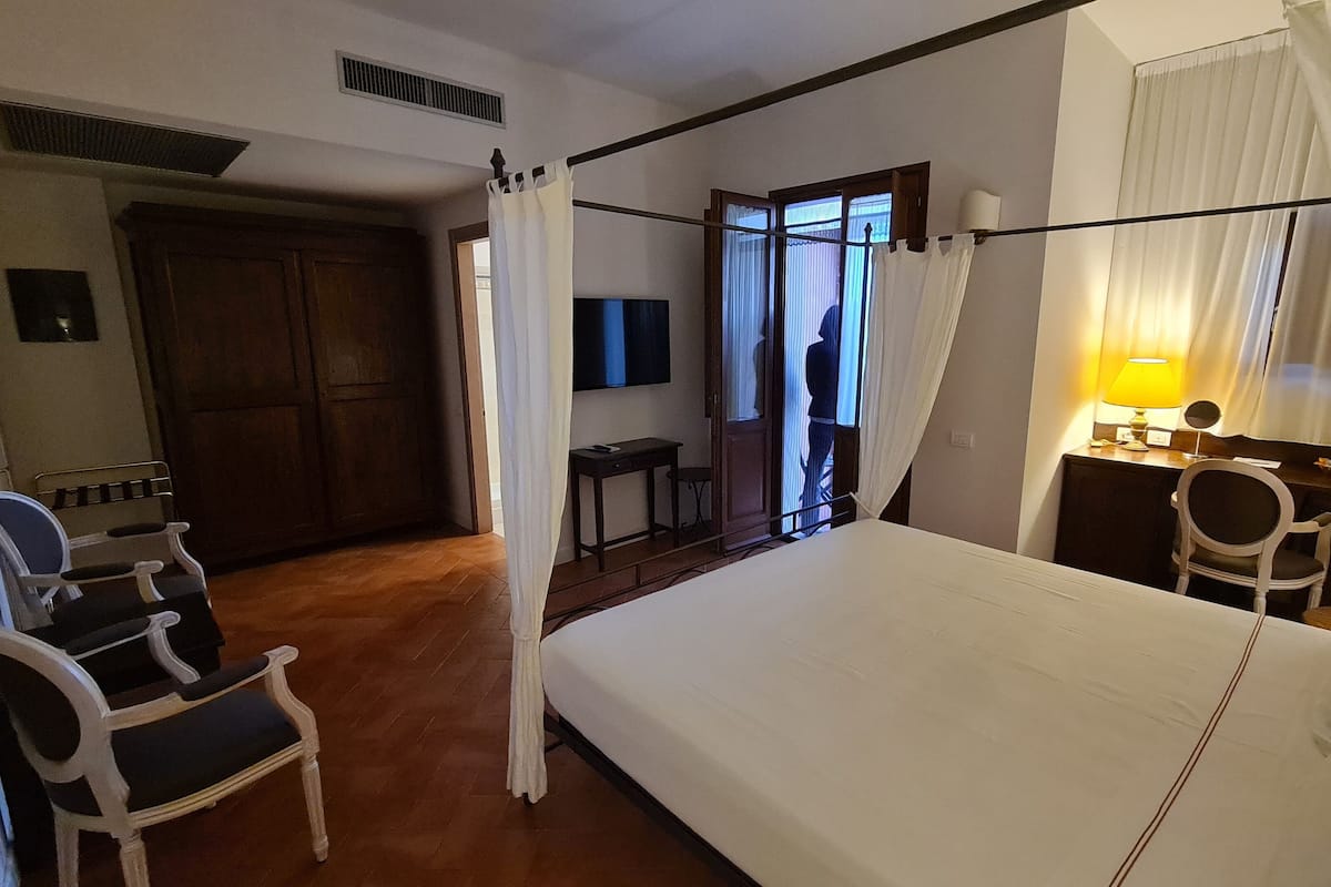 Une chambre d’hôtel avec un lit, un bureau, une chaise, une armoire et une fenêtre avec des rideaux.