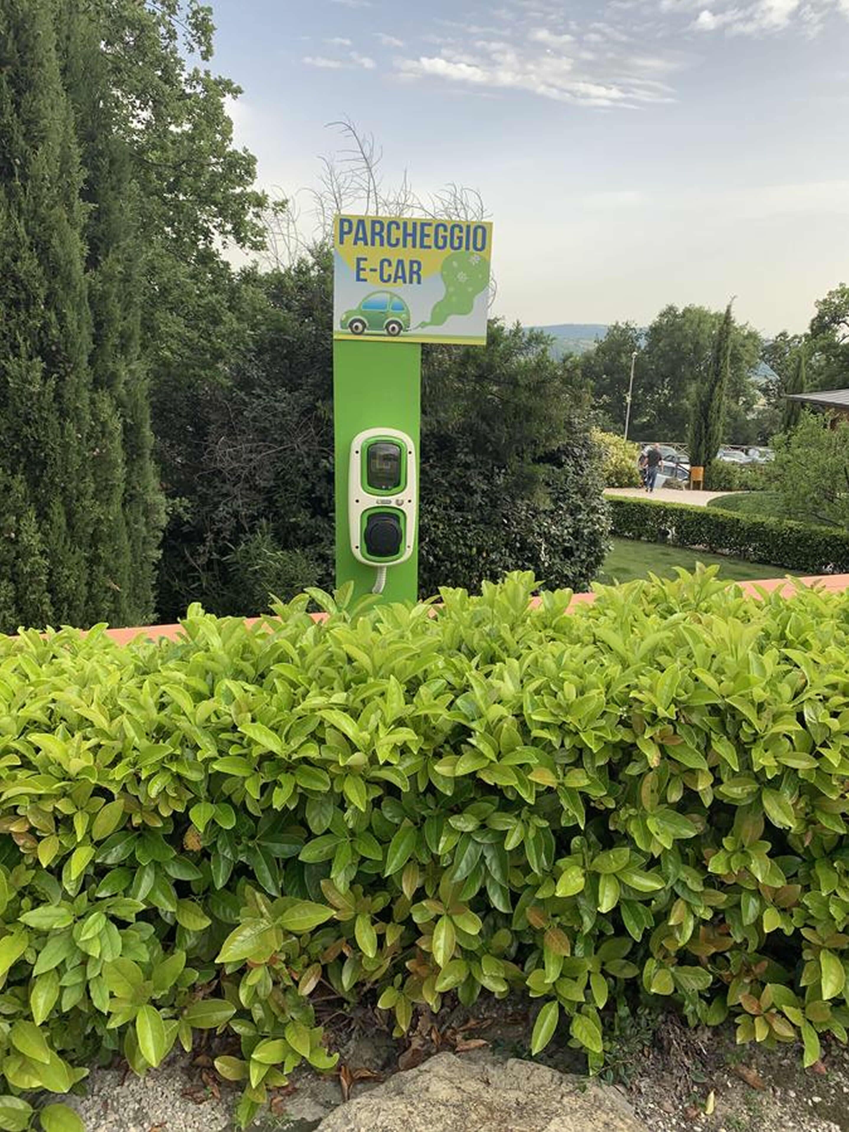 A green electric car charging station with a sign that reads "PARCHEGGIO E-CAR" and a map of Italy.