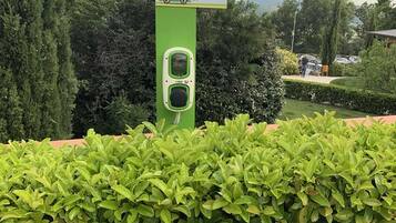 Une borne de recharge pour voitures électriques, de couleur verte, avec une pancarte indiquant « PARCHEGGIO E-CAR » et une carte de l’Italie.