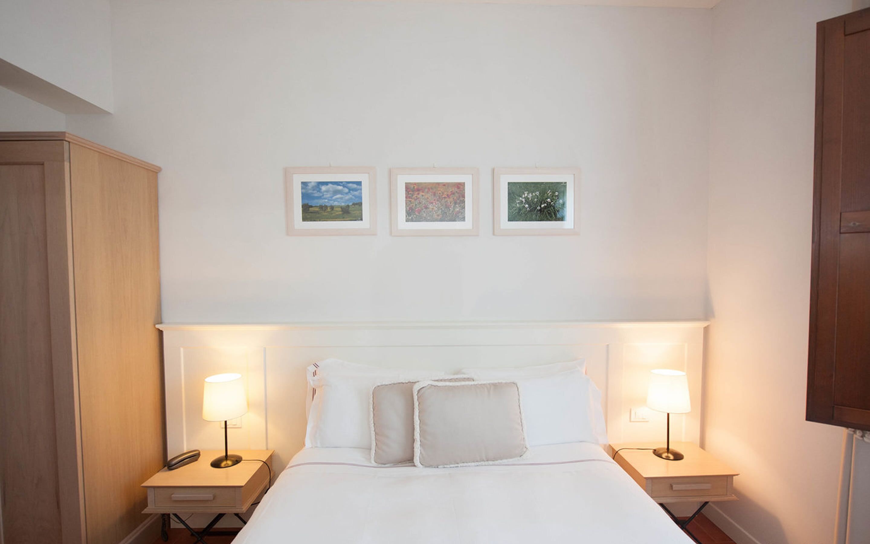 A hotel room with a large bed, two bedside tables with lamps, and three framed pictures on the wall.