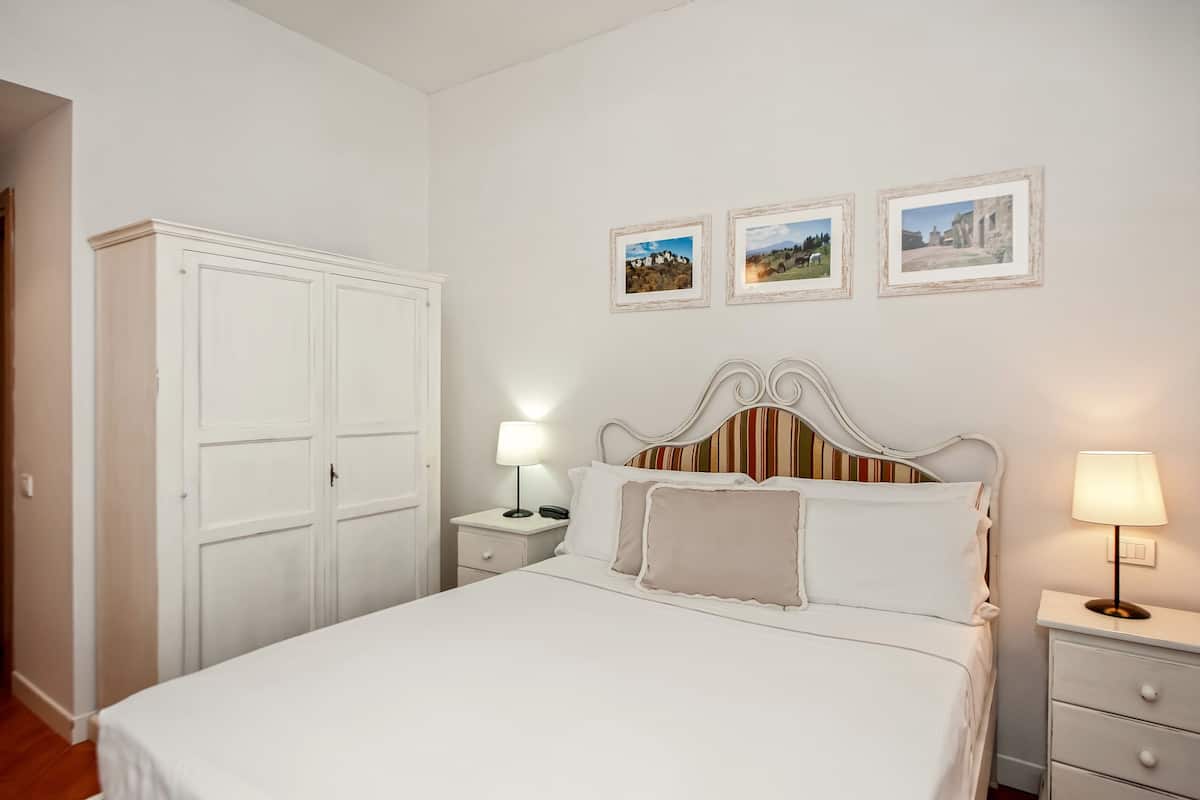 Une chambre à coucher bien rangée, avec un lit, des tables de chevet, une armoire et trois tableaux encadrés accrochés au mur.