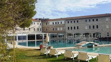 A hotel with a swimming pool, lounge chairs, and a stone building with multiple windows.