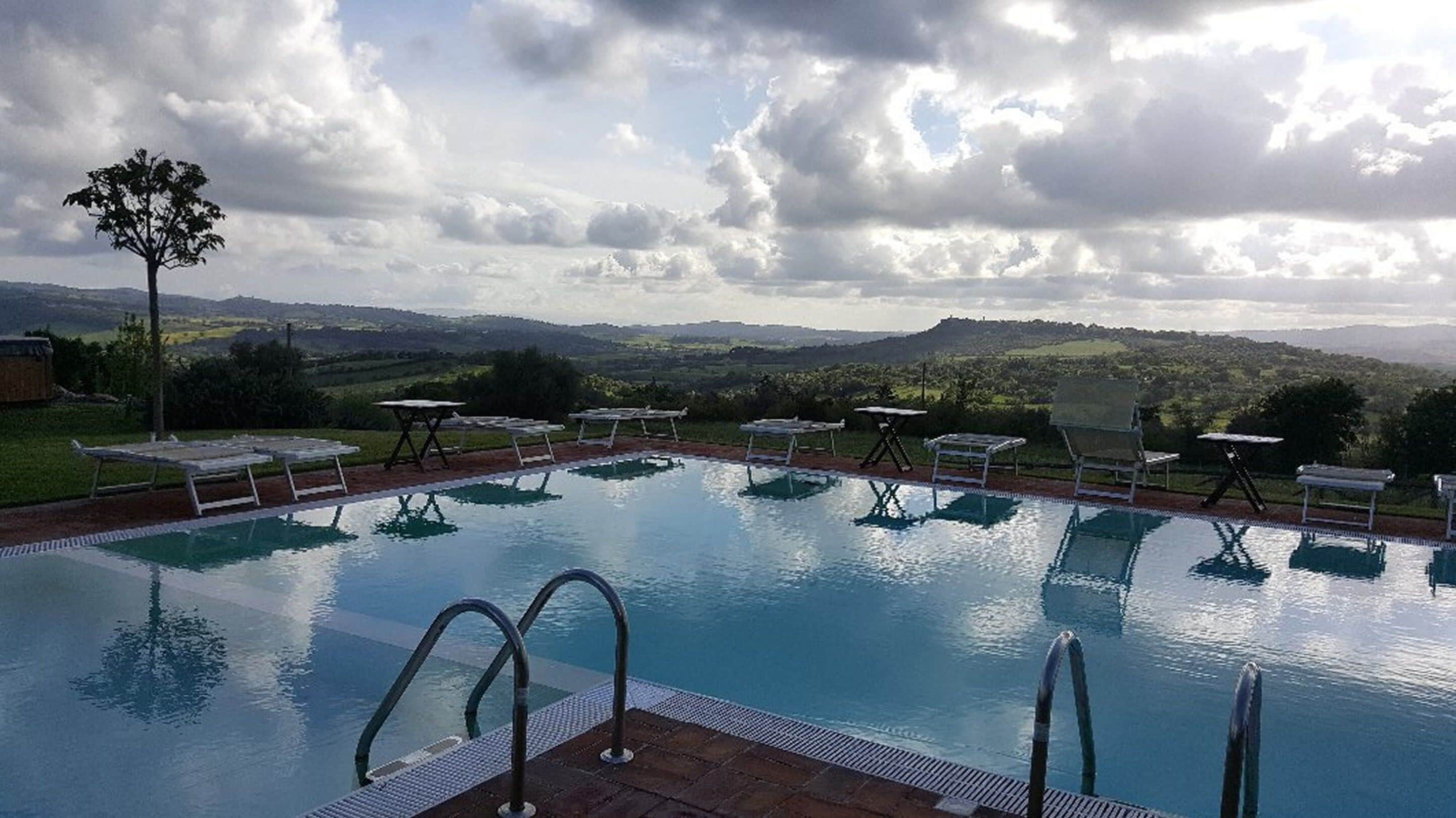 A swimming pool with lounge chairs and tables, surrounded by a scenic landscape.