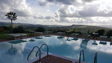 A swimming pool with lounge chairs and tables, surrounded by a scenic landscape.