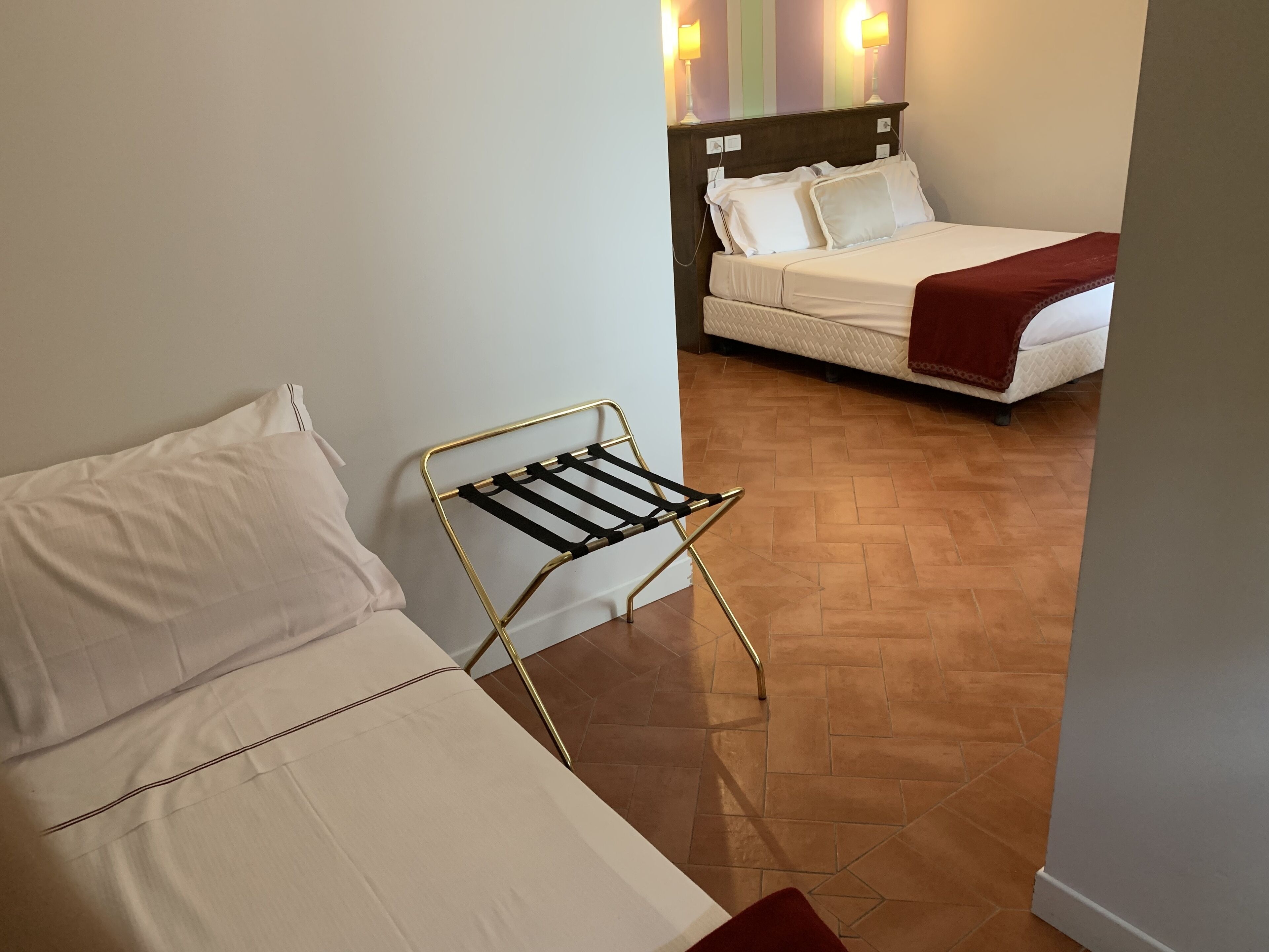 A hotel room with a bed, a small table with a drying rack, and a wooden floor.