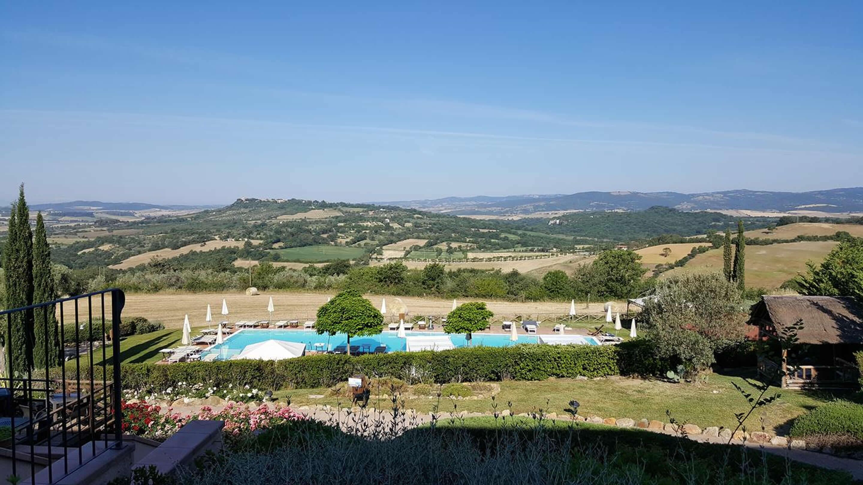 Un espace piscine agrémenté de chaises longues et de parasols, entouré de jardins bien entretenus et offrant une vue panoramique sur des collines verdoyantes et des montagnes lointaines.