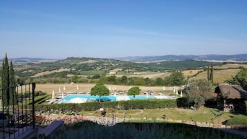 Un espace piscine agrémenté de chaises longues et de parasols, entouré de jardins bien entretenus et offrant une vue panoramique sur des collines verdoyantes et des montagnes lointaines.