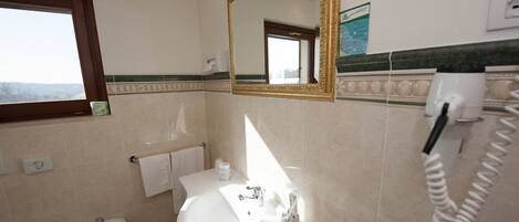 A bathroom with a sink, bidet, and a mirror. There is a towel rack and a hand dryer on the wall.