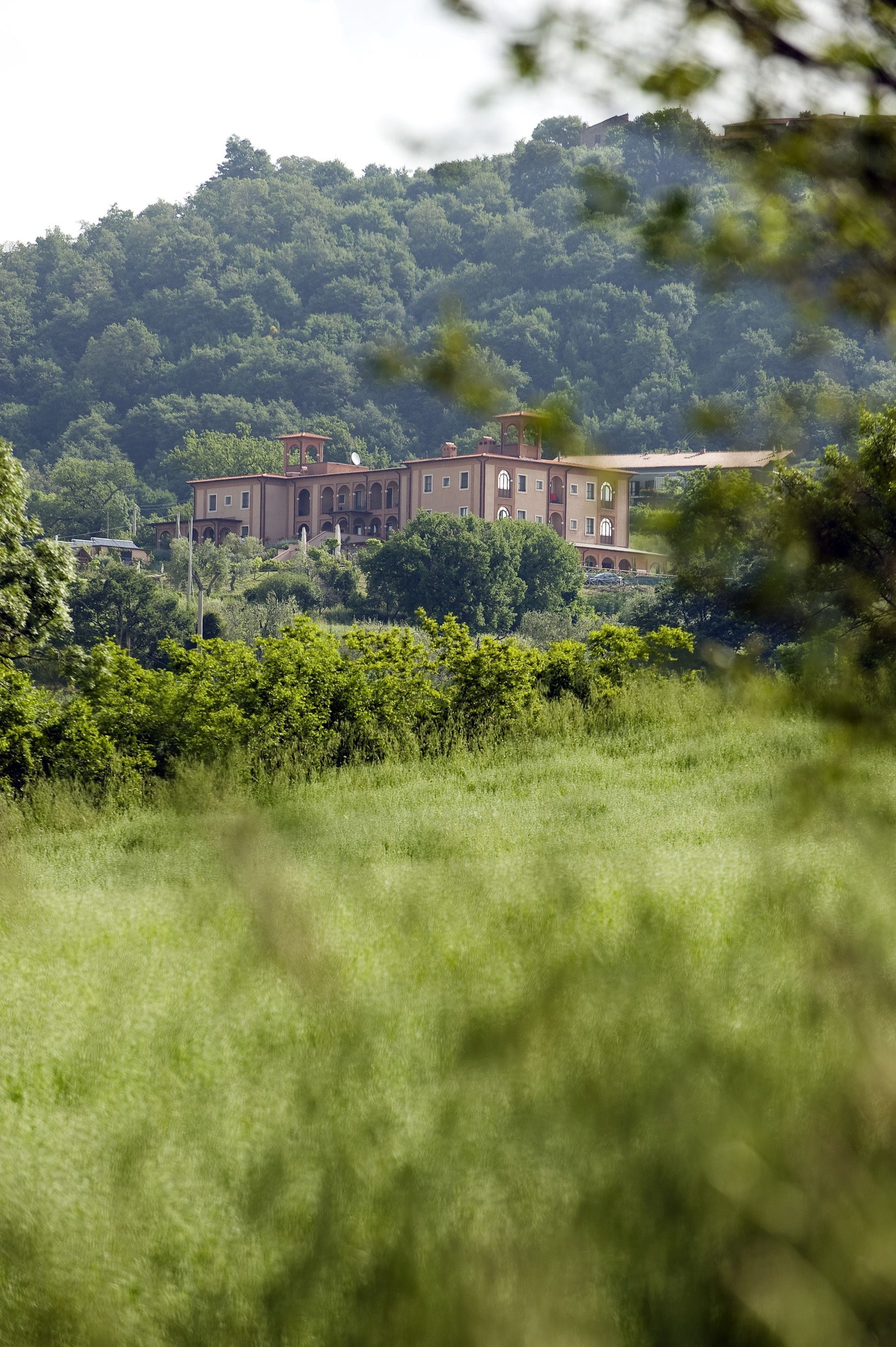 A large, multi-story building with a symmetrical facade, surrounded by lush greenery and hills in the background.