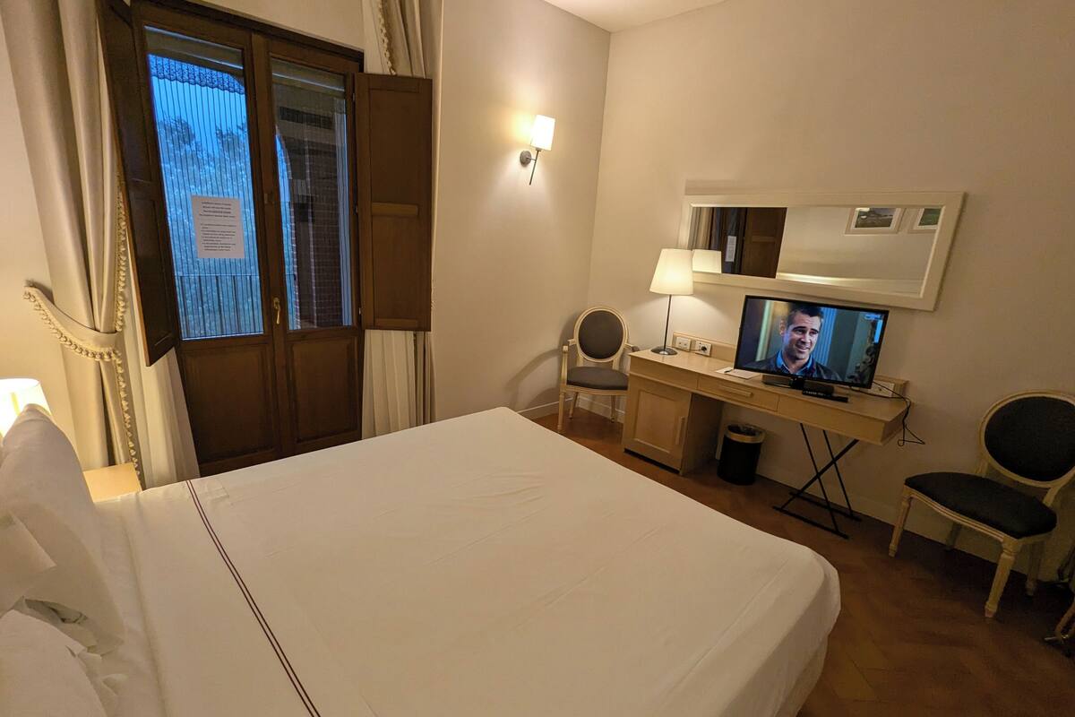 Une chambre d’hôtel avec un lit, un bureau, une télévision et une fenêtre avec des rideaux.