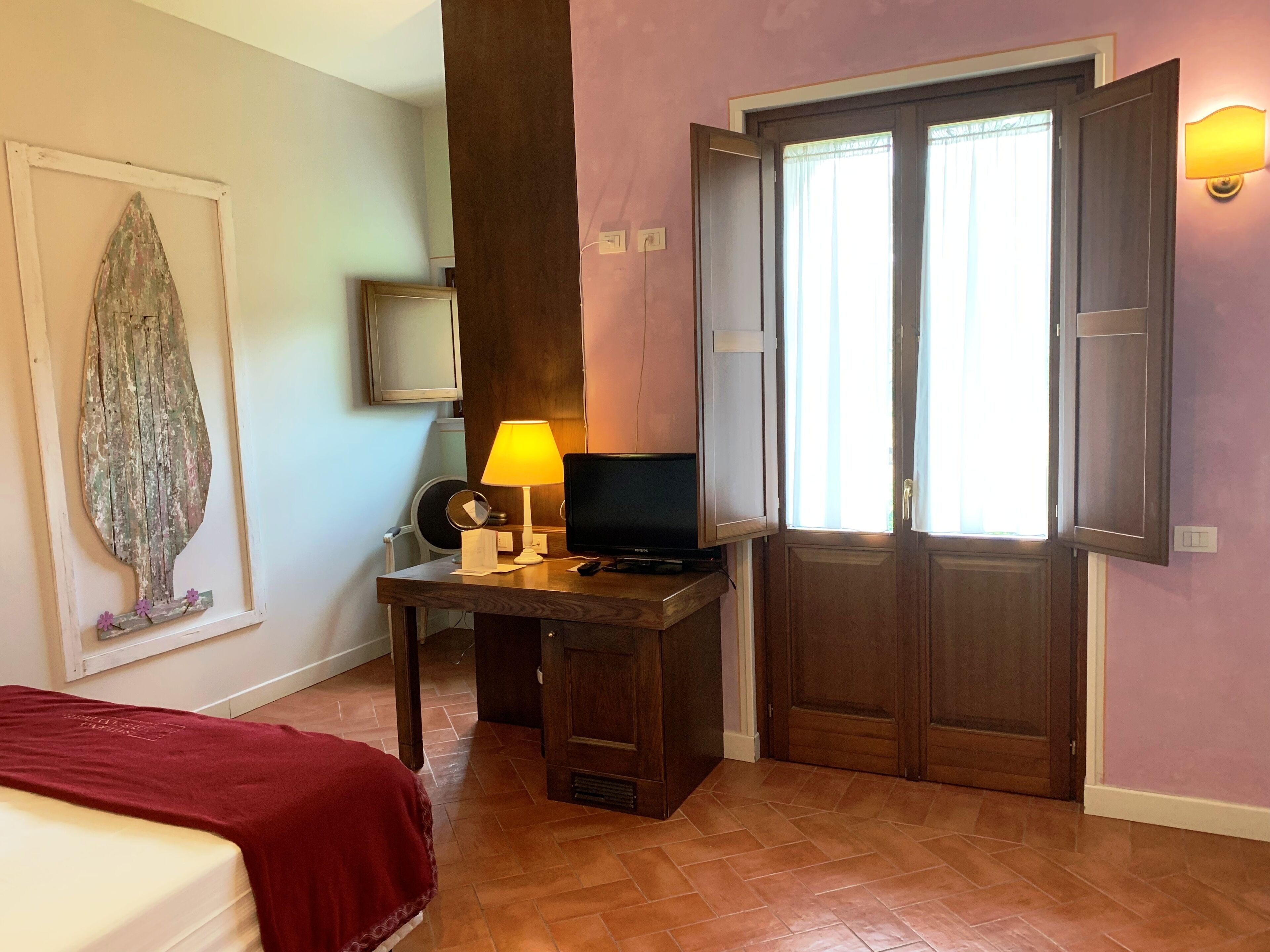 Een hotelkamer met een houten bureau, een televisie, een lamp, een spiegel en een bed met een rode deken.