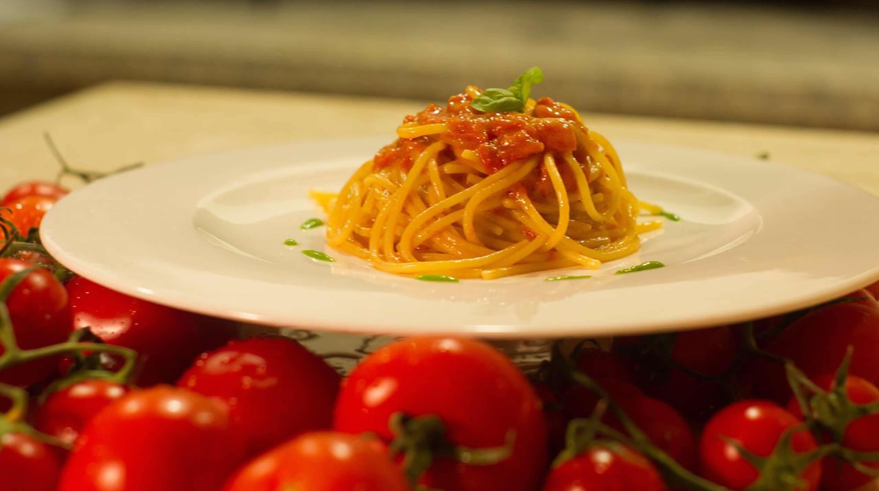 Un plato de espagueti con salsa de tomate, adornado con hierbas y rodeado de tomates frescos.