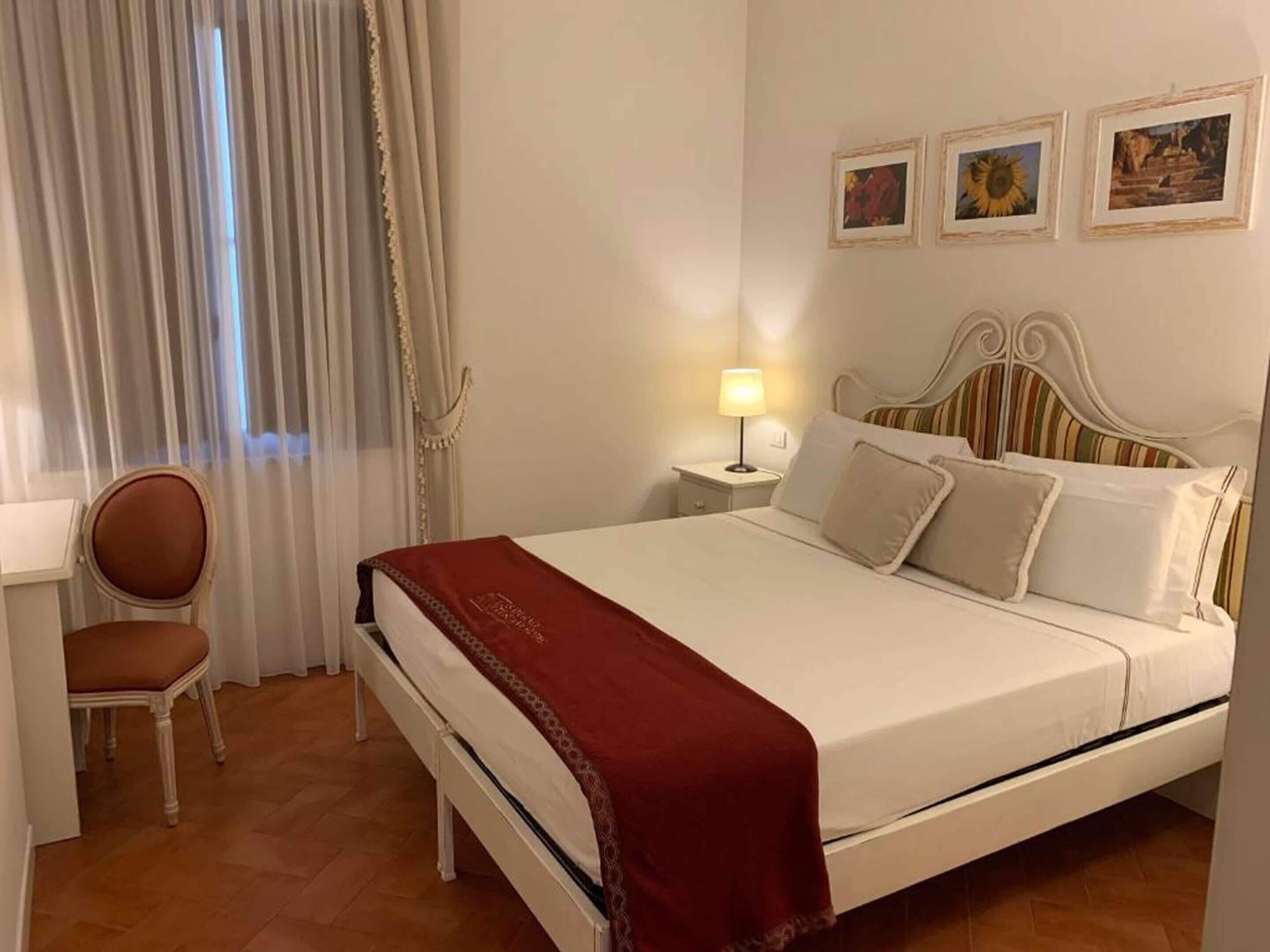 Une chambre d’hôtel avec un lit, une chaise, une table de chevet avec une lampe et trois tableaux encadrés accrochés au mur.