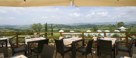 Un área de comedor al aire libre con mesas y sillas, con vistas a una piscina y un paisaje pintoresco.