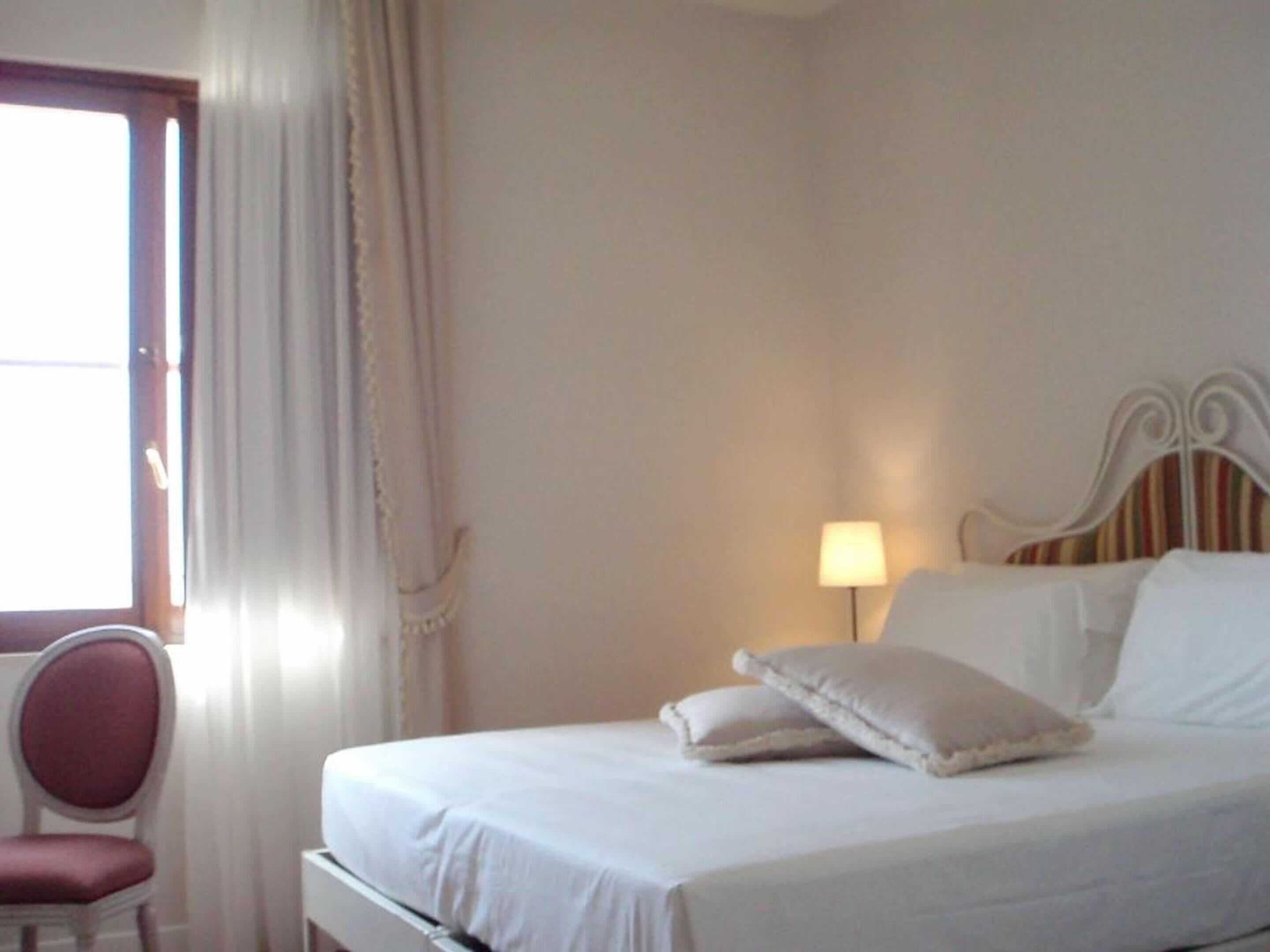 Een hotelkamer met een bed, een stoel, een lamp en een raam met gordijnen.
